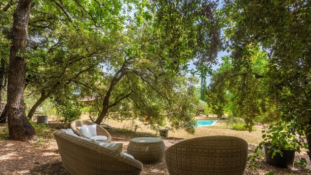 Wicker furniture under a tree, a pool in the background, and a garden setting. - Les Lilas Guest Room with Shared Pool, Garden, Summer Kitchen, and Wi-Fi (Carcès)