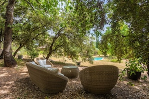 Wicker furniture under a tree, a pool in the background, and a garden setting. - Bed and Breakfast 'Les Lilas' with Shared Pool, Shared Terrace and Wi-Fi (Carcès)