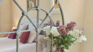 A bed with a metal headboard, a bedside table with a vase of flowers, and a wall-mounted mirror. - Les Lilas Guest Room with Shared Pool, Garden, Summer Kitchen, and Wi-Fi (Carcès)