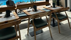 Un restaurante con terraza, vista a la piscina y un edificio moderno al fondo.