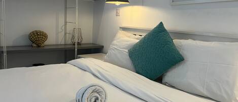 A neatly made bed with a rolled towel, a teal pillow, and a lamp on a bedside table.