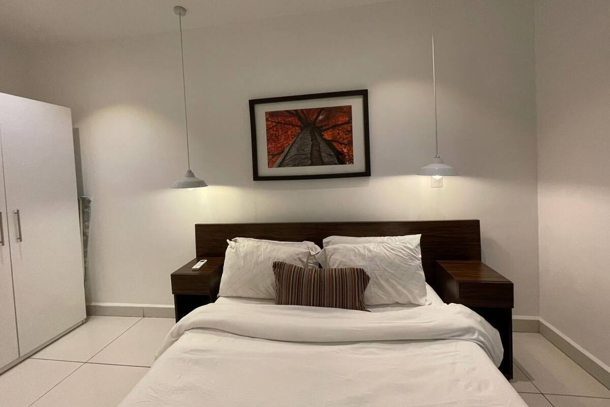 A neatly made bed with white linens, a wooden headboard, and two bedside lamps.