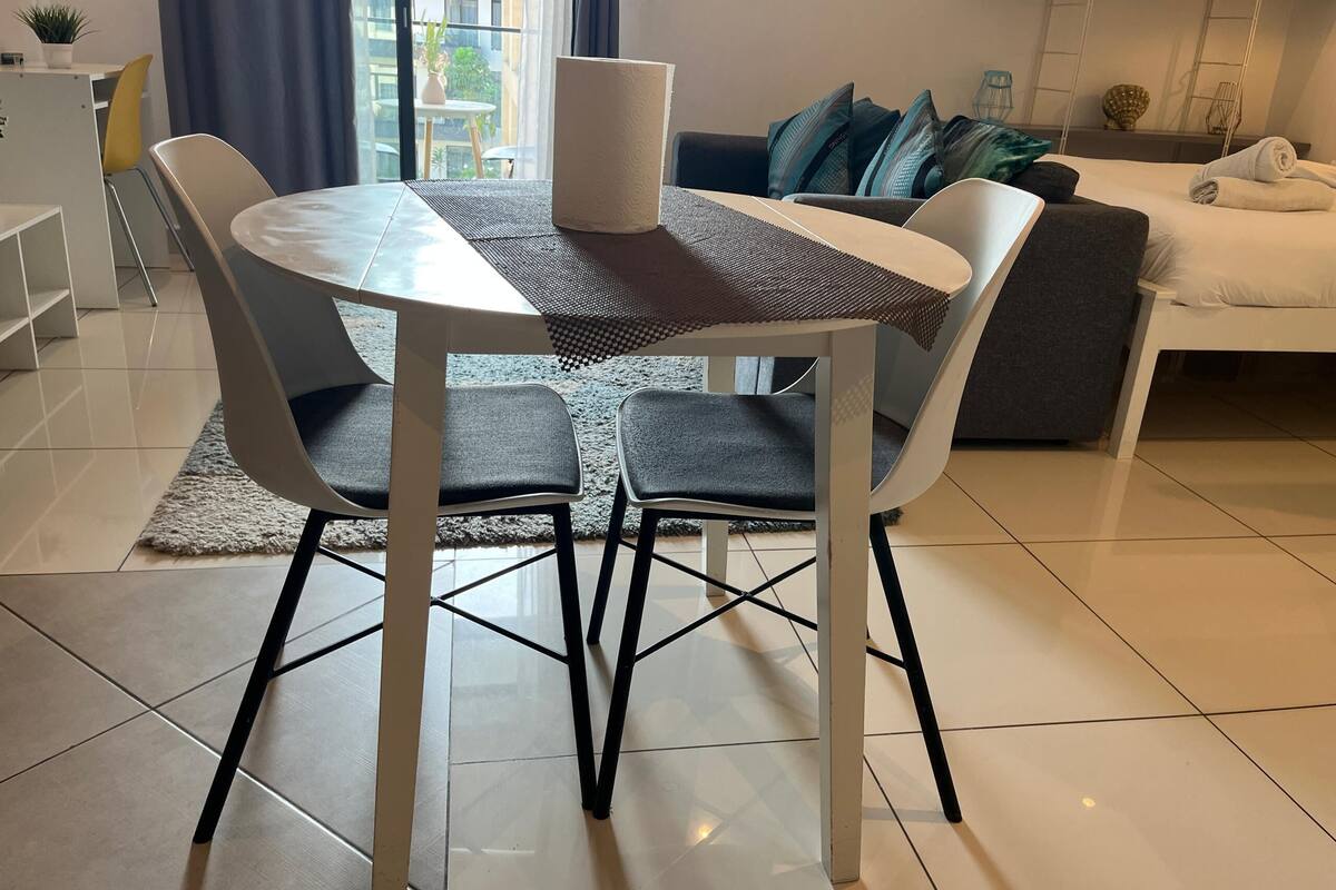 A modern dining area with a round table, two chairs, a coffee table, and a view of the outside balcony.