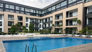 Un edificio moderno con piscina central, varios balcones y abundante vegetación.