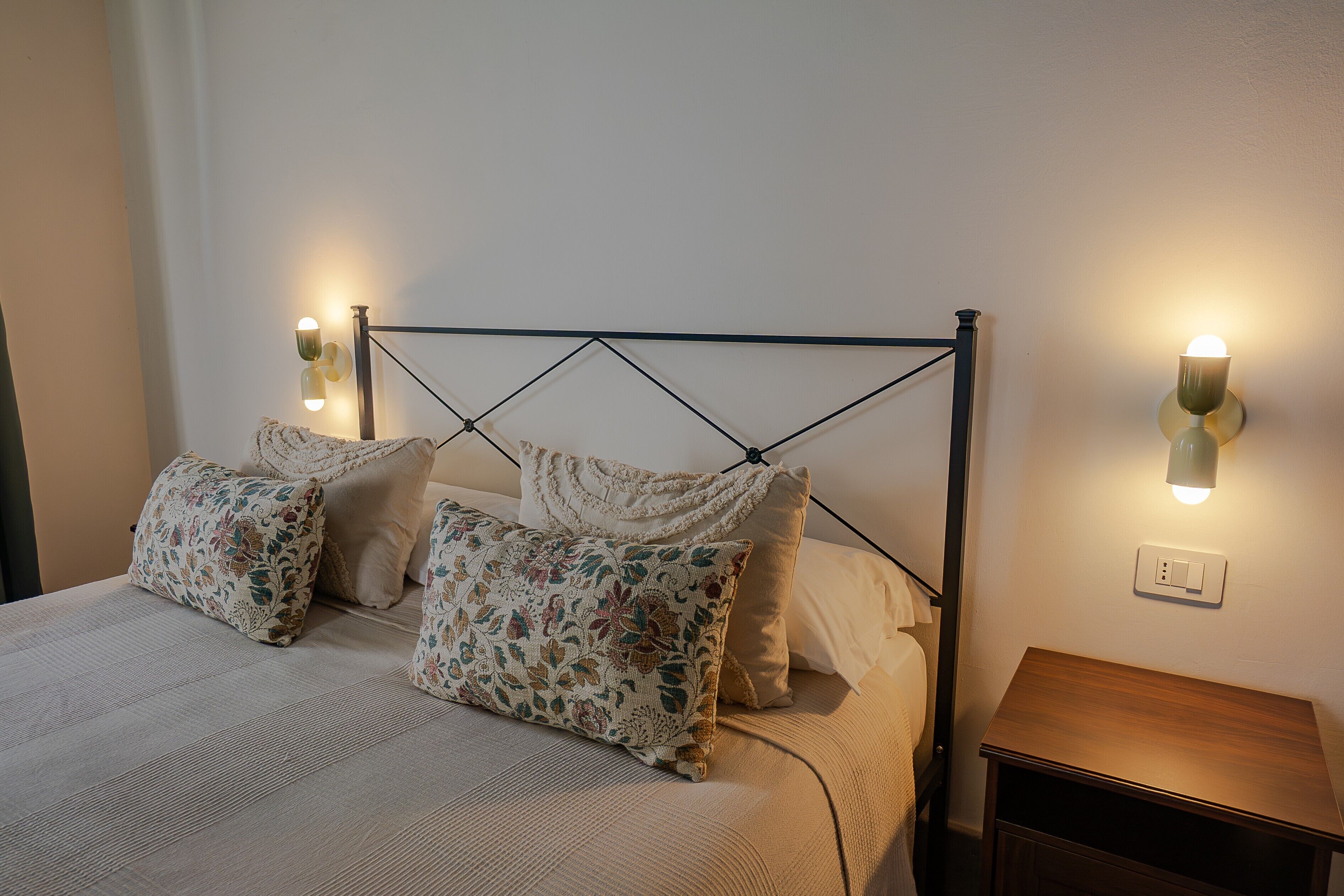 Un lit avec des oreillers à motifs floraux, une tête de lit en métal et des lampes de chevet.