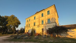 Un bâtiment à deux étages doté d’une façade symétrique, de nombreuses fenêtres avec des volets verts et d’une allée gravillonnée.
