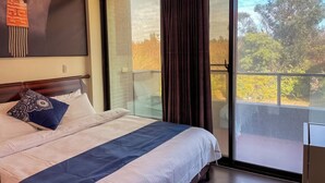 Habitación de hotel con una cama grande, vista a árboles a través de una puerta corrediza de vidrio y una pared con diseño decorativo.