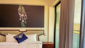 Habitación de hotel con una cama grande, una mesita de noche, una obra de arte en la pared y un ventanal con cortinas.