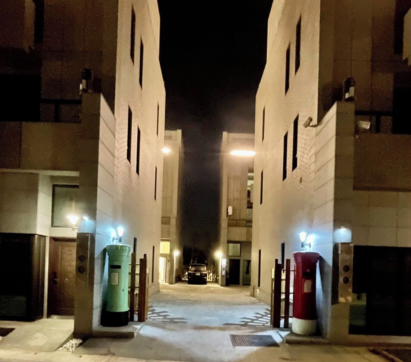 A nighttime view of a building entrance with two illuminated bollards and a car parked inside.
