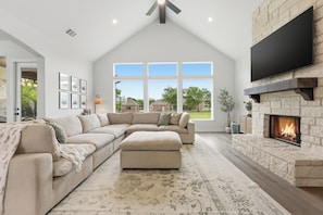 A spacious living room with a large sectional sofa, a fireplace, and a large window providing a view of the outside. - LUXE COUNTRY FARMHOUSE with over 1 acre, dogs OK, 4bd, 3 ba fully furnished! (Gunter)