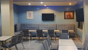 A restaurant with a blue wall, a sofa, tables, chairs, a TV, and speakers.