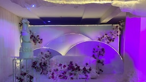 A stage with a tiered cake, floral arrangements, and a seating area.
