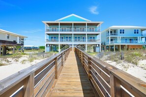 Eine Holzpromenade führt zu einem Strandhotel mit mehreren Balkonen und einem blauen Dach.