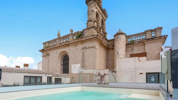 Um edifício histórico com piscina, uma torre alta e uma entrada em arco imponente.