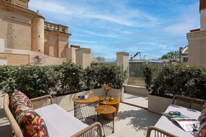 Una terraza en la azotea con mobiliario exterior, vista panorámica de la ciudad y un edificio de ladrillo al fondo.