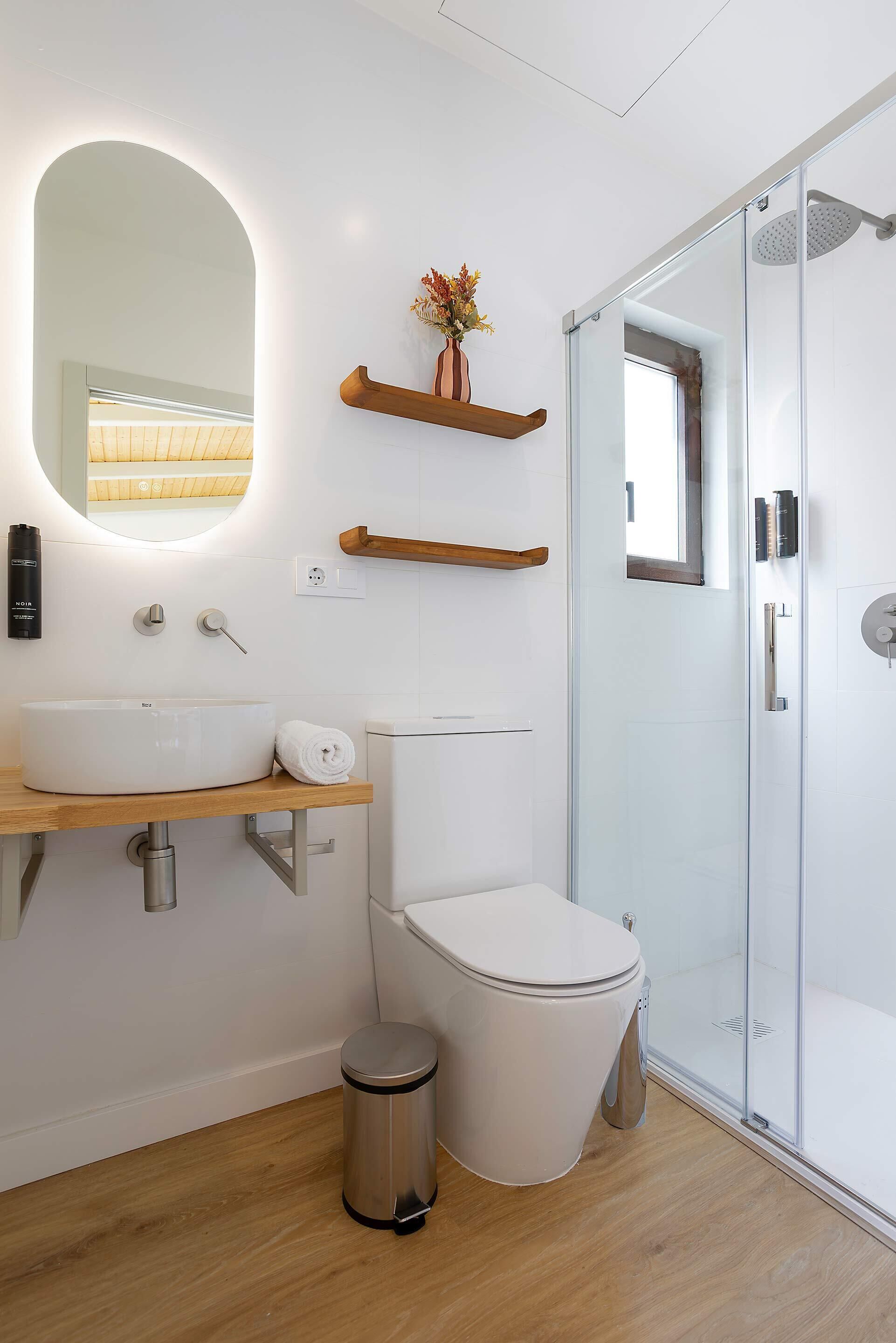 A modern bathroom with a large oval sink, a toilet, a glass shower enclosure, and wooden shelves above the sink.