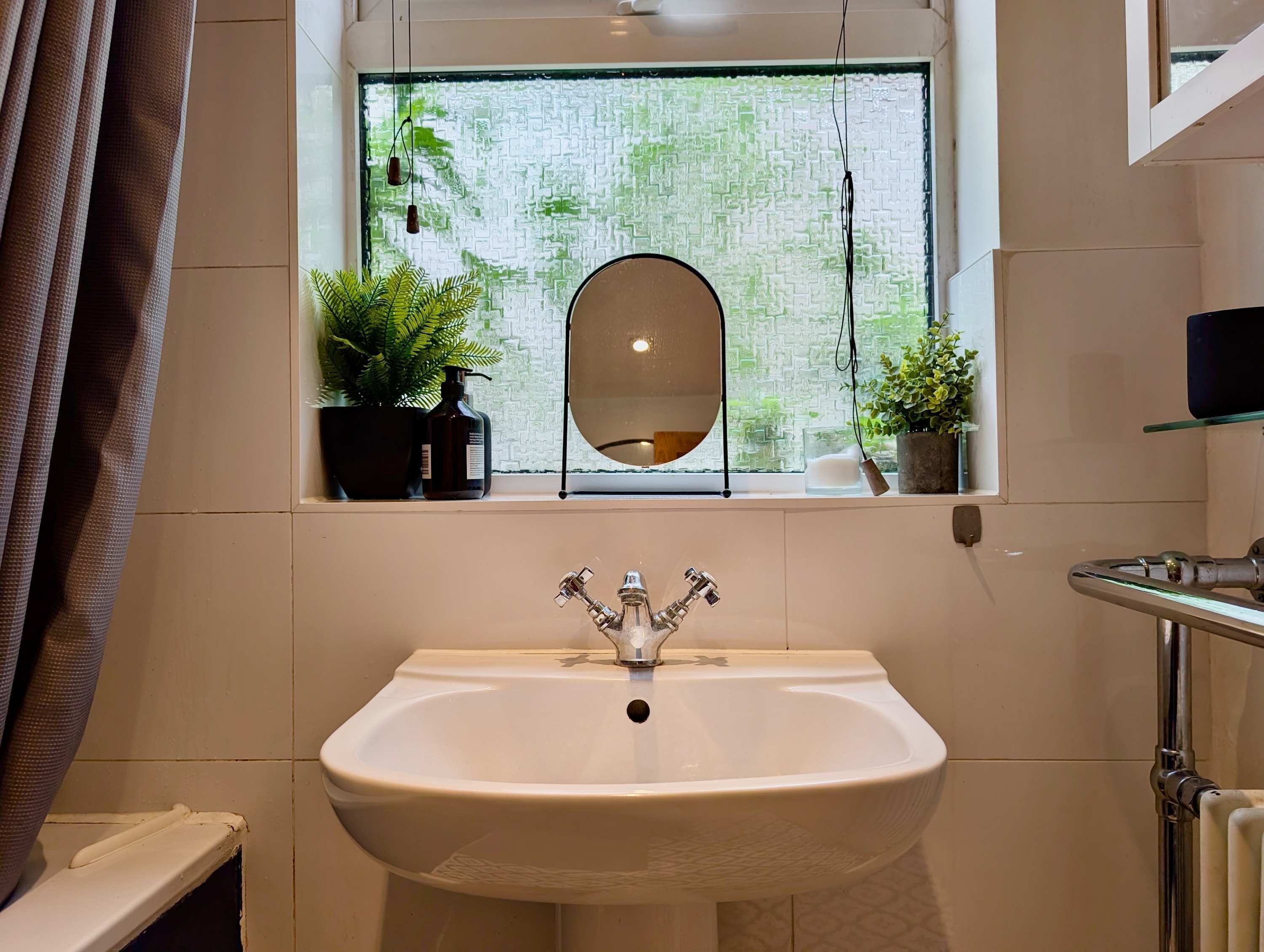 A bathroom with a white sink, a window with a view of greenery, and a mirror above the sink.