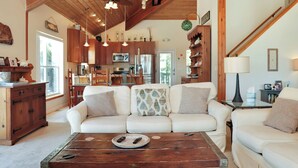 Amplia sala de estar con sofá blanco, mesa de centro de madera y cocina al fondo.