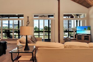 Ein Wohnzimmer mit einer Couch, einem Couchtisch, einer Lampe, einem Fernseher und Blick auf Palmen und Gebäude durch große Fenster.