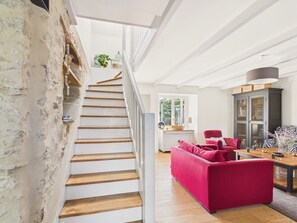 A staircase with wooden steps and white railings, leading to a living area with a red sofa, a wooden table, and a cabinet with glass doors. - House with garden, 4 adults 1 child (Pleurtuit)