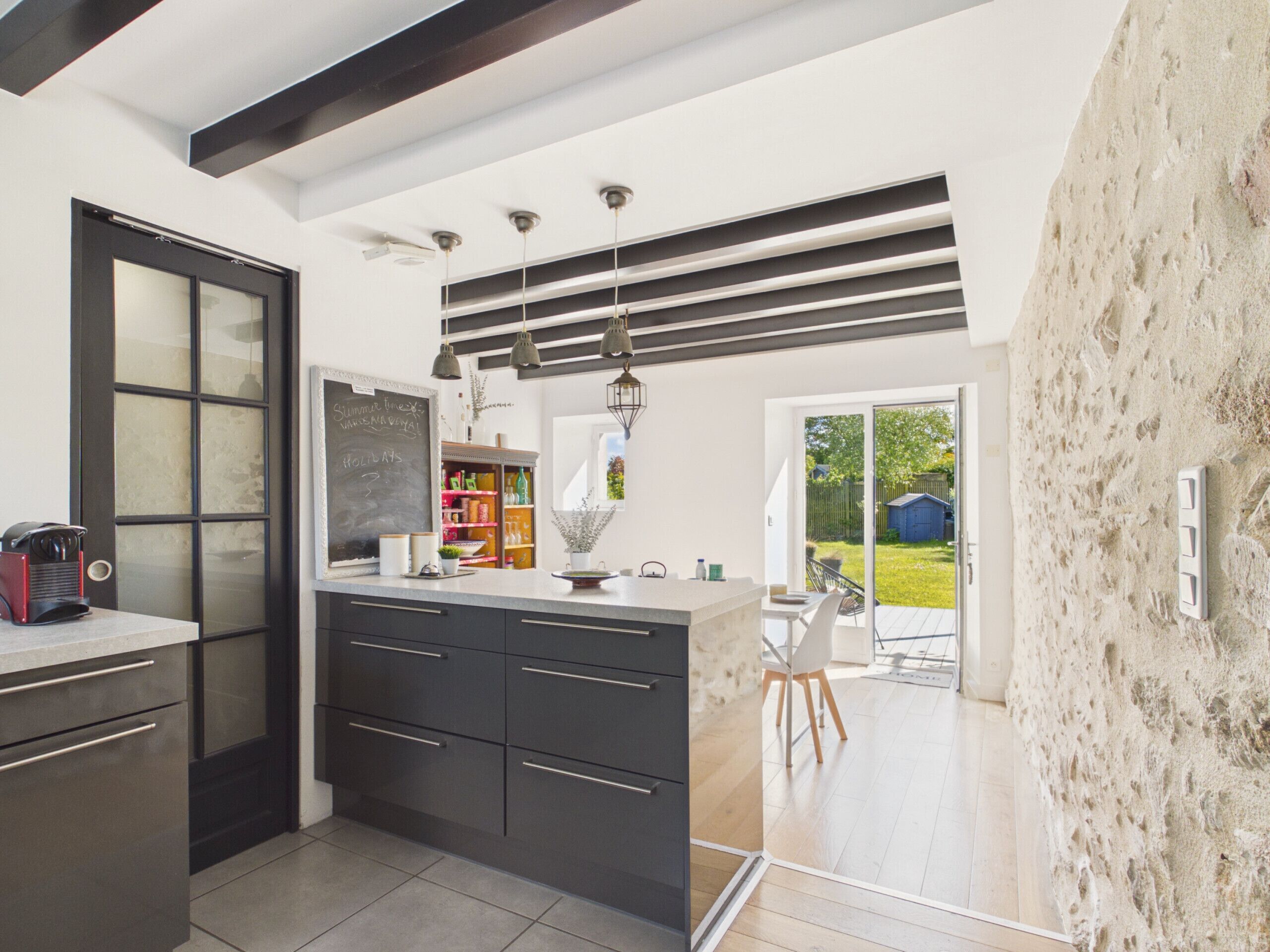 A modern kitchen with dark cabinetry, a chalkboard, and a view to the outdoor patio.