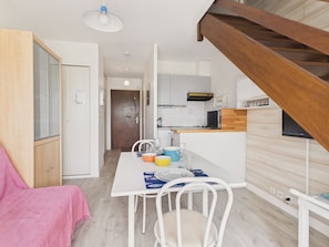 Eine kleine Küche mit Essbereich, einer Holztreppe und Blick auf das Wohnzimmer.