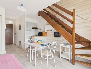 Eine moderne Küche mit weißen Schränken, einer Holztreppe und einem Essbereich mit weißen Stühlen und einem rosa Teppich.