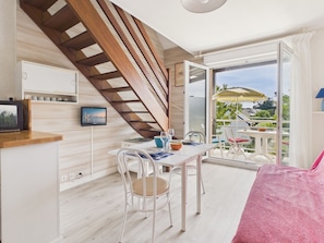 Ein modernes Zimmer mit einer Holztreppe, einem Essbereich inklusive Tisch und Stühlen, einem an der Wand befestigten Fernseher und einer Glastür, die zu einem Außenbereich mit Tisch und Sonnenschirm führt.