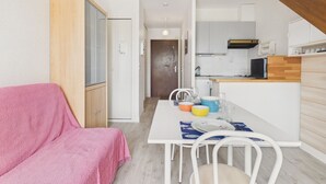 Kompakti oleskelutila, jossa on pieni keittiönurkkaus, ruokailualue ja pieni oleskelualue, jossa on vaaleanpunainen viltti.