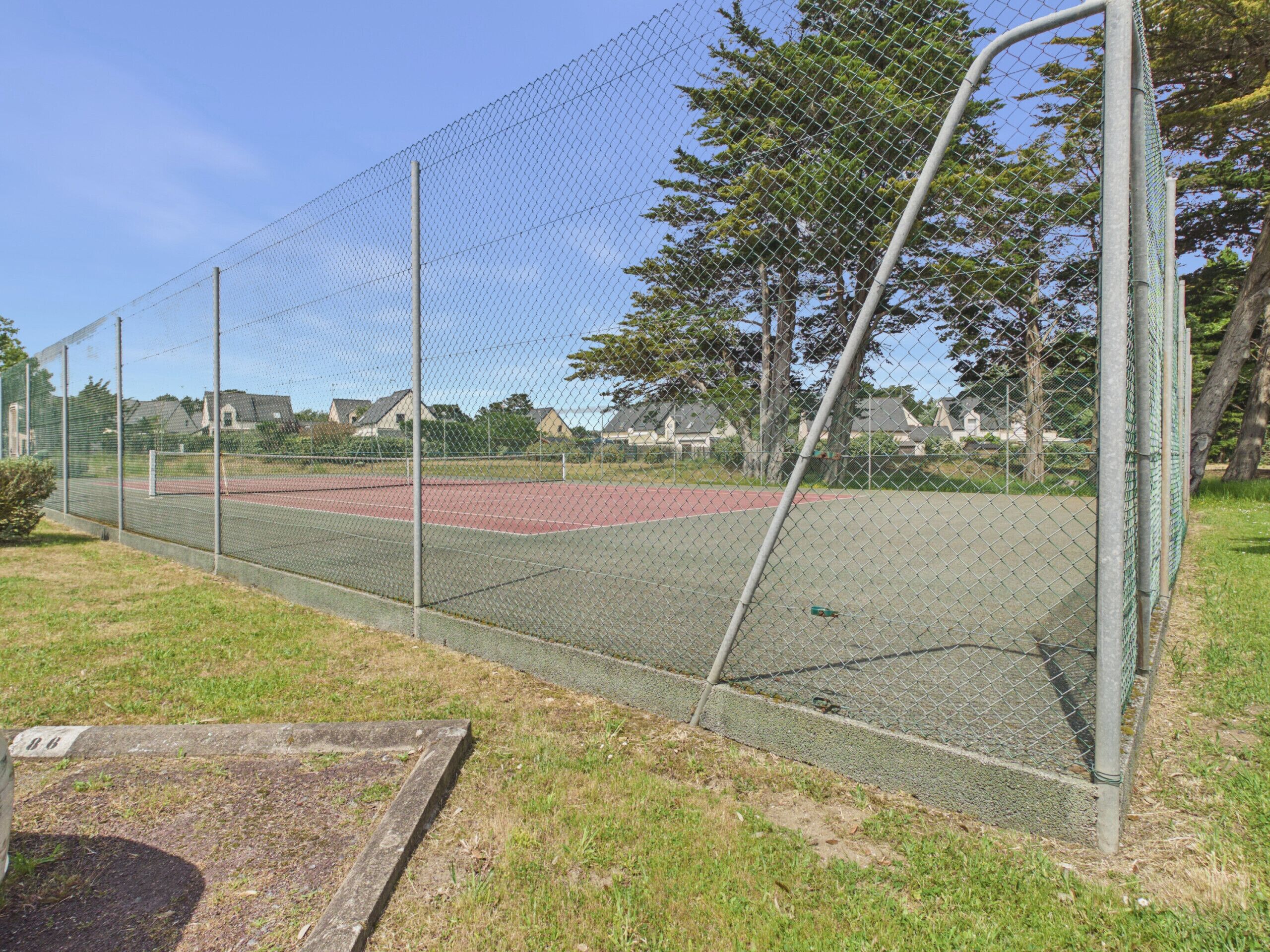 A fenced sports court with a chain-link fence, a metal pole, and a grassy area with a concrete structure.