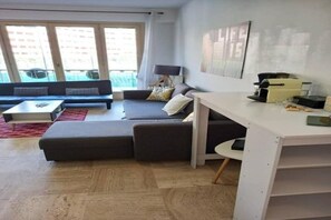 Ein modernes Wohnzimmer mit einer Couch, einem Couchtisch, einem Schreibtisch und einem großen Fenster.