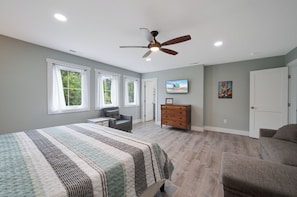 A bedroom with a bed, a ceiling fan, a dresser, a TV, and a door.