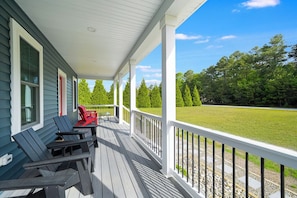A covered porch with outdoor seating, a view of a green field, and a house with white trim.