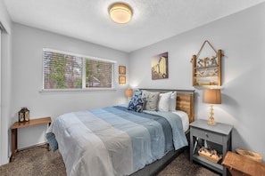 A bedroom with a bed, bedside tables, a lamp, a wall decoration, and a window with blinds.