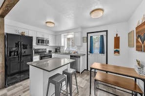 A modern kitchen with a central island, stainless steel appliances, and a wooden dining table.