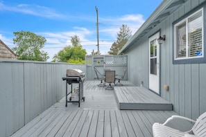 A deck with a grill, chairs, and a small table.