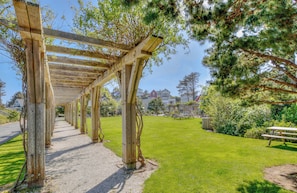 A wooden pergola walkway in a park with picnic tables and a house in the background. - Ocean View Luxury Olivia Beach Home, Top-Deck Hot Tub! (Lincoln City)