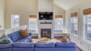 Ein Wohnzimmer mit blauem Sofa, Kamin und großen Fenstern mit Jalousien.