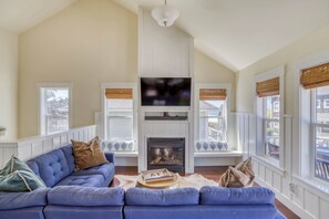 Ein Wohnzimmer mit blauem Sofa, Kamin und großen Fenstern mit Jalousien.