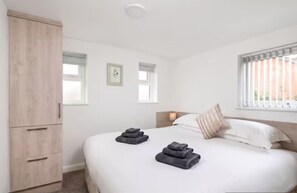 Un dormitorio con una cama, un armario, dos ventanas y cabecero con almohada.