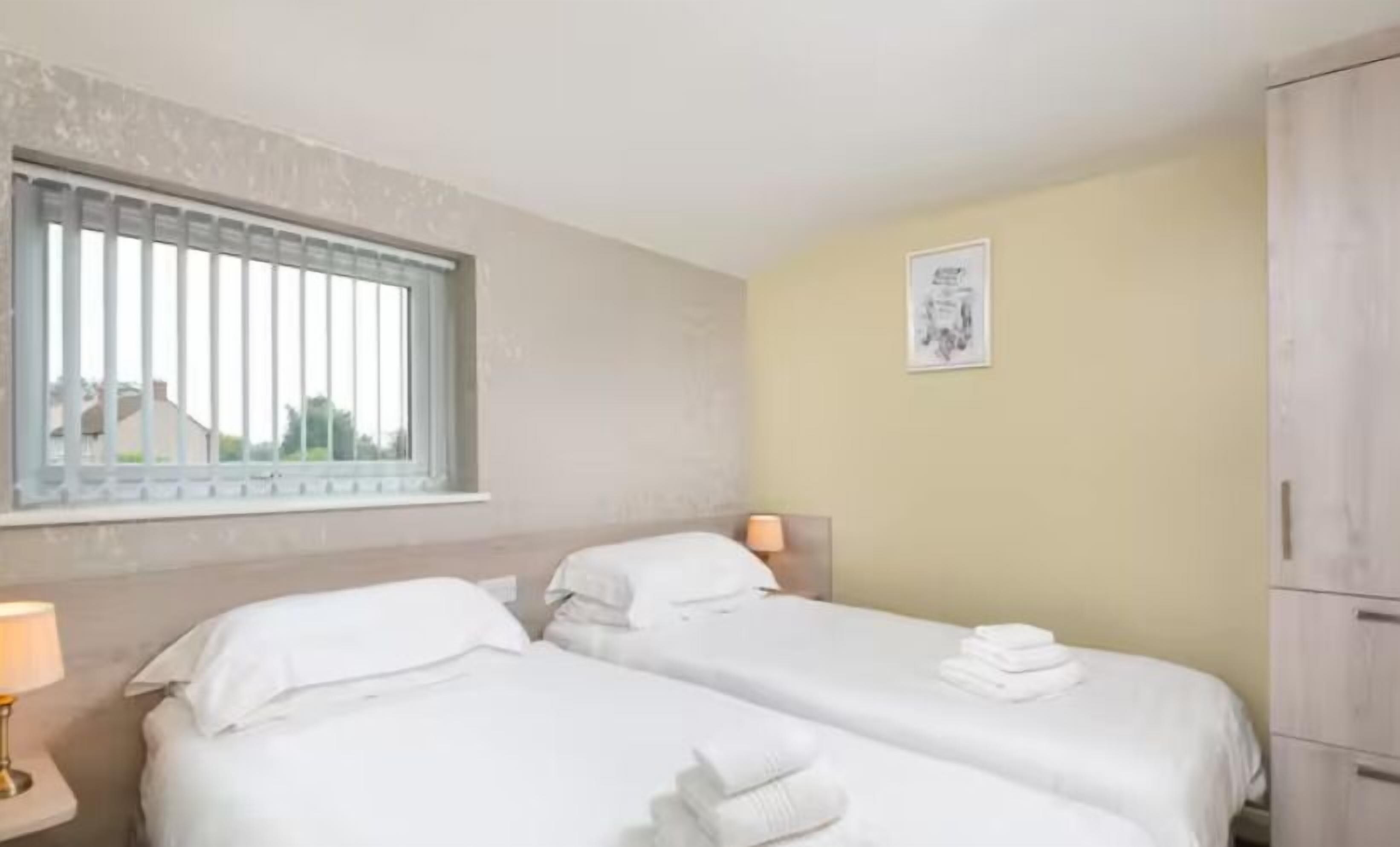 Habitación de hotel con dos camas, una ventana con persianas, una lámpara de noche, un cuadro enmarcado en la pared y un armario.