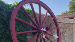 A large red wheel with a flower in the center, leaning against a wall with green foliage. - The Chestnut (Chadurie)