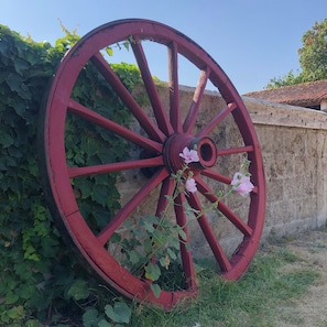 A large red wheel with a flower in the center, leaning against a wall with green foliage. - The Chestnut (Chadurie)