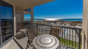A balcony with a view of the beach, a round table, and two wicker chairs. - Phoenix X 202 1 Bedroom Condo (Orange Beach)