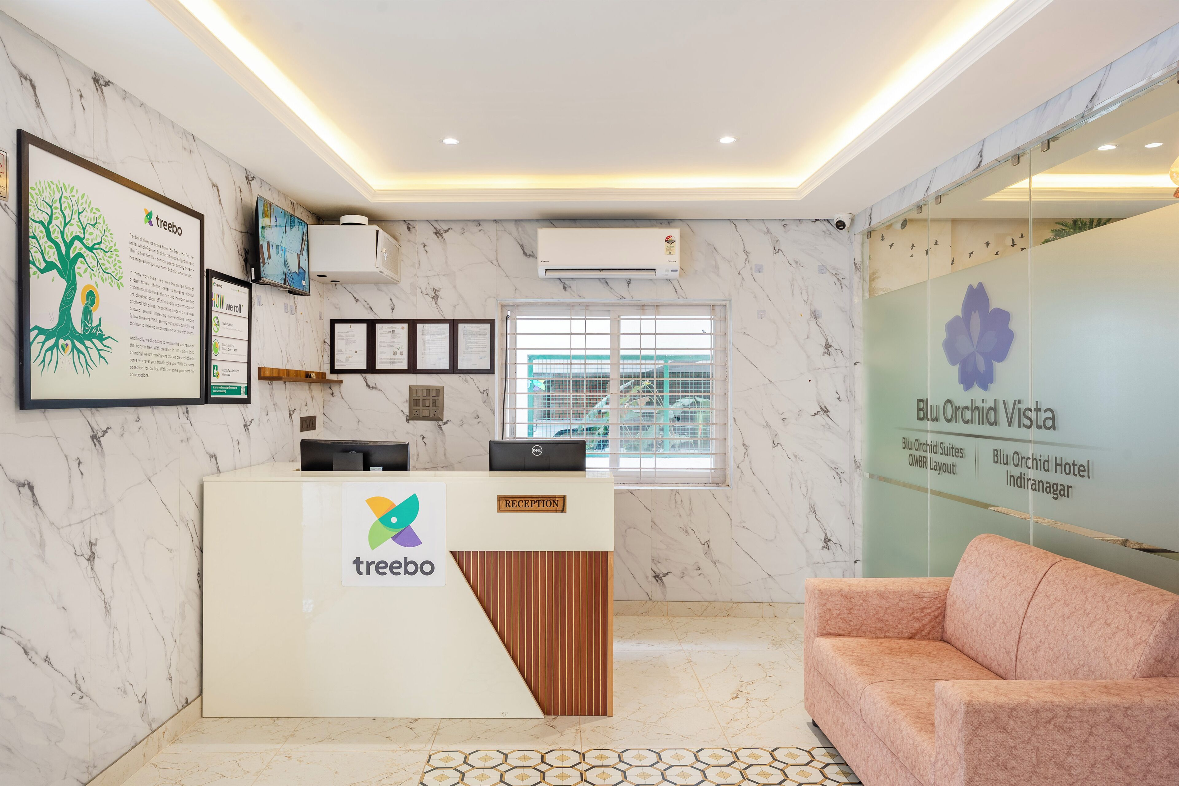 A reception desk with a tree logo, a window with a view, and a wall with hotel names.