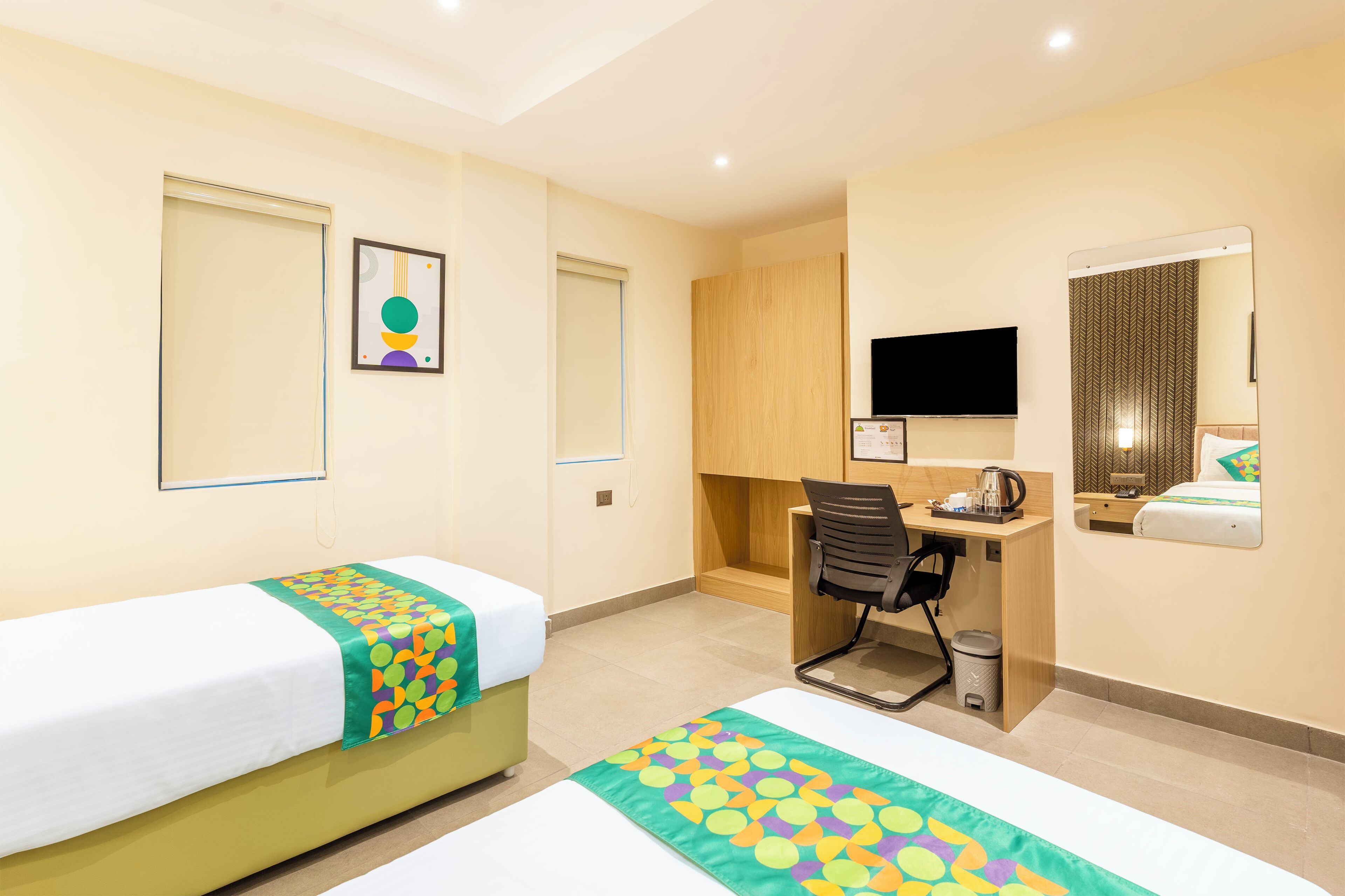 A hotel room with two beds, a desk, a chair, a television, and a mirror.