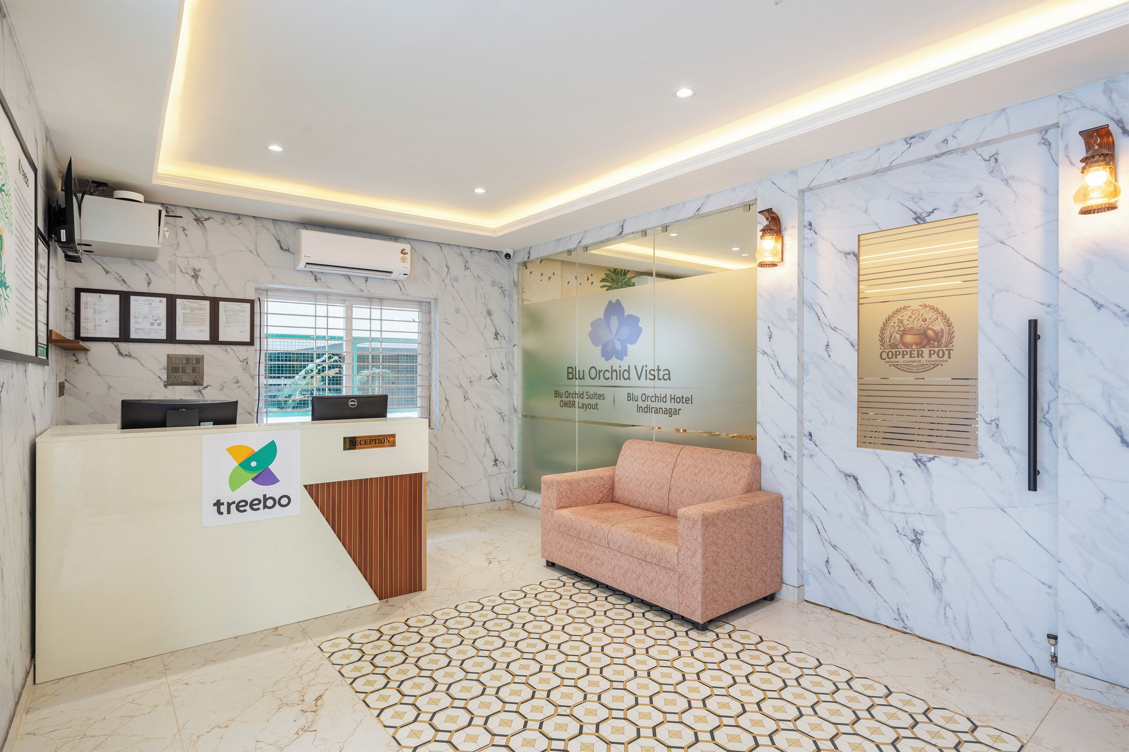 A reception desk with a logo, a marble wall, a sofa, and a sign for Blu Orchid Vista hotel.