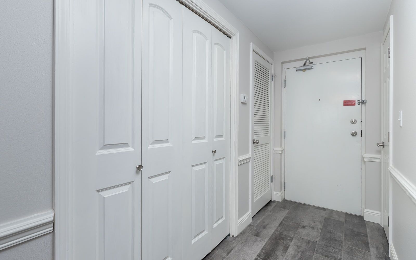 A hallway with white doors, a vent, and a red sign on one door.