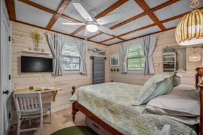 A room with a bed, a desk, a chair, a ceiling fan, and a TV mounted on the wall.