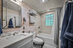Une salle de bain avec un mur en bois, un grand miroir, un lavabo, des toilettes et une baignoire.